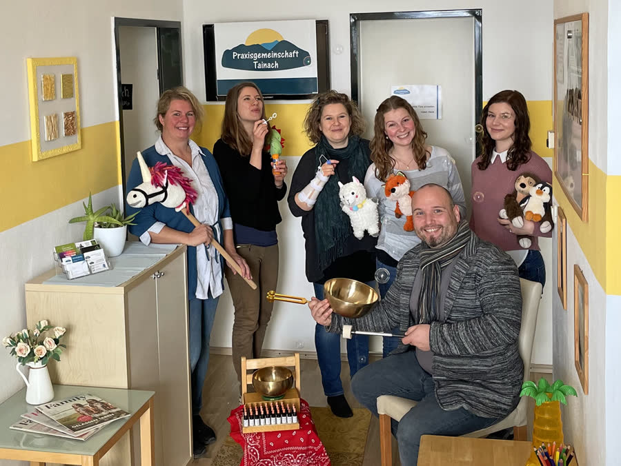 Das Team der Praxisgemeinschaft Tainach im Eingangsbereich der Praxis, mit Plüschtieren, Stockpferd und Klangschalen